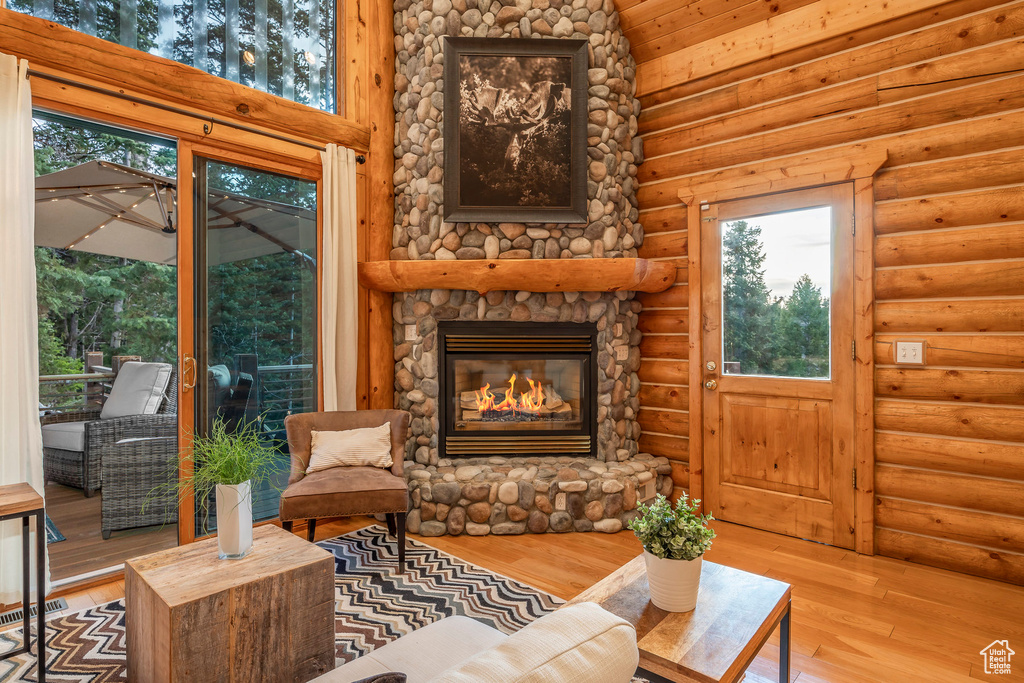 Living room featuring a stone fireplace, log walls, and hardwood / wood-style floors