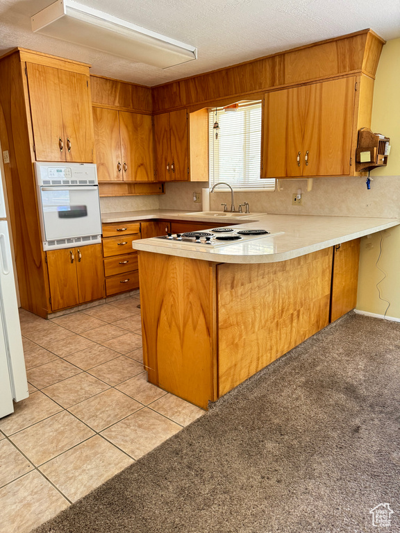 Kitchen with kitchen peninsula, white appliances, and light tile floors