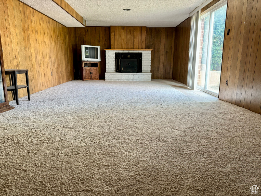 Unfurnished living room featuring a healthy amount of sunlight, wooden walls, a fireplace, and carpet floors