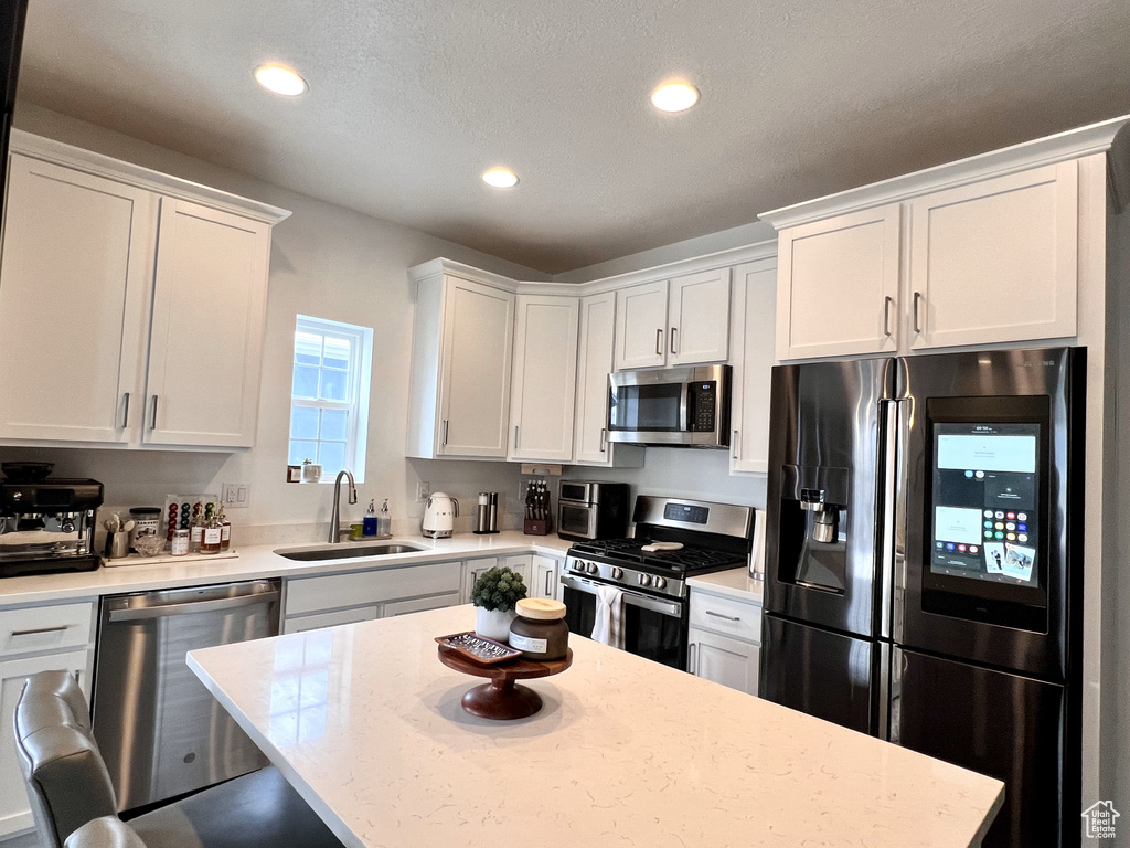 Kitchen with stainless steel appliances, white cabinets, sink, and light stone countertops