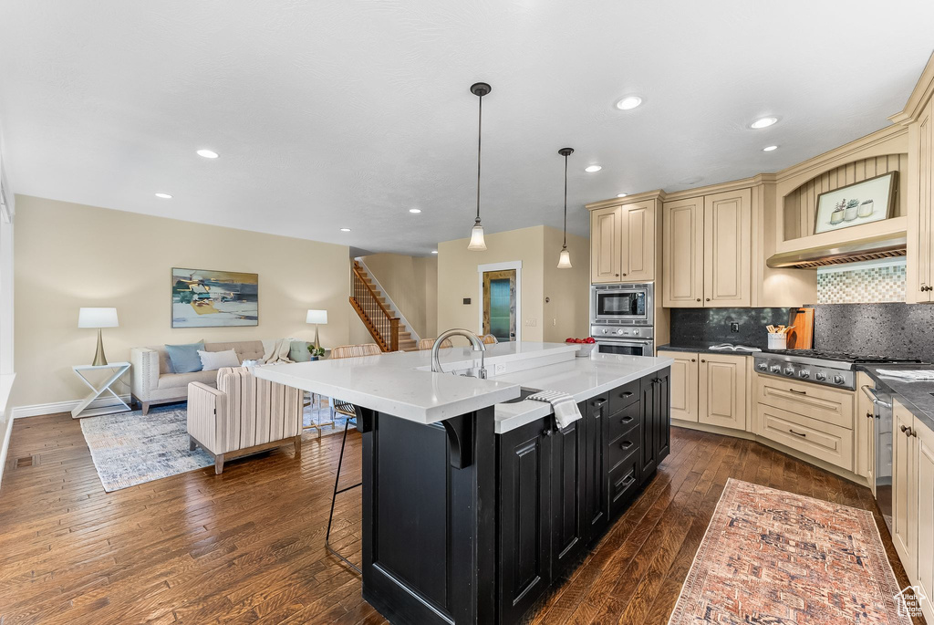 Kitchen with backsplash, cream cabinets, appliances with stainless steel finishes, and dark hardwood / wood-style flooring