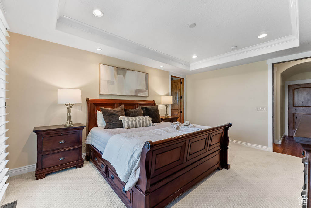 Bedroom with light carpet, ornamental molding, and a tray ceiling