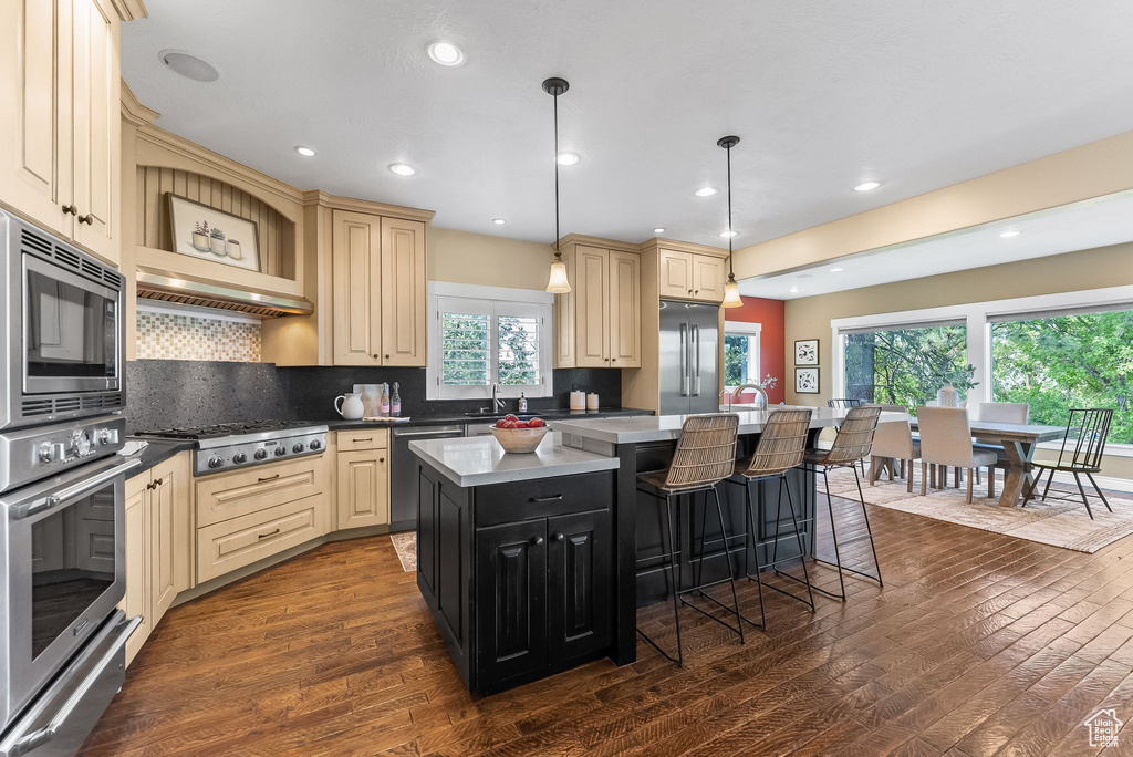 Kitchen featuring pendant lighting, dark wood-type flooring, backsplash, appliances with stainless steel finishes, and a kitchen island