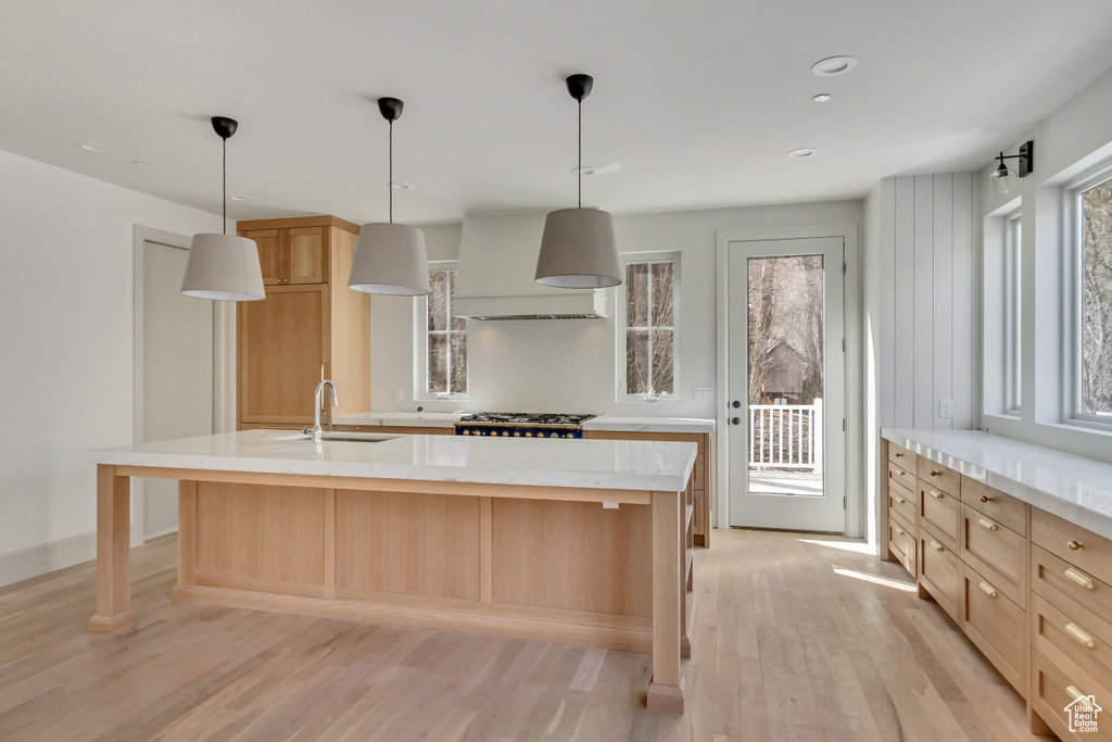 Kitchen with custom exhaust hood, a kitchen island with sink, sink, pendant lighting, and light wood-type flooring