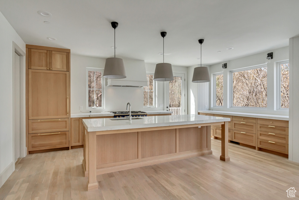 Kitchen featuring premium range hood, light hardwood / wood-style flooring, an island with sink, and decorative light fixtures
