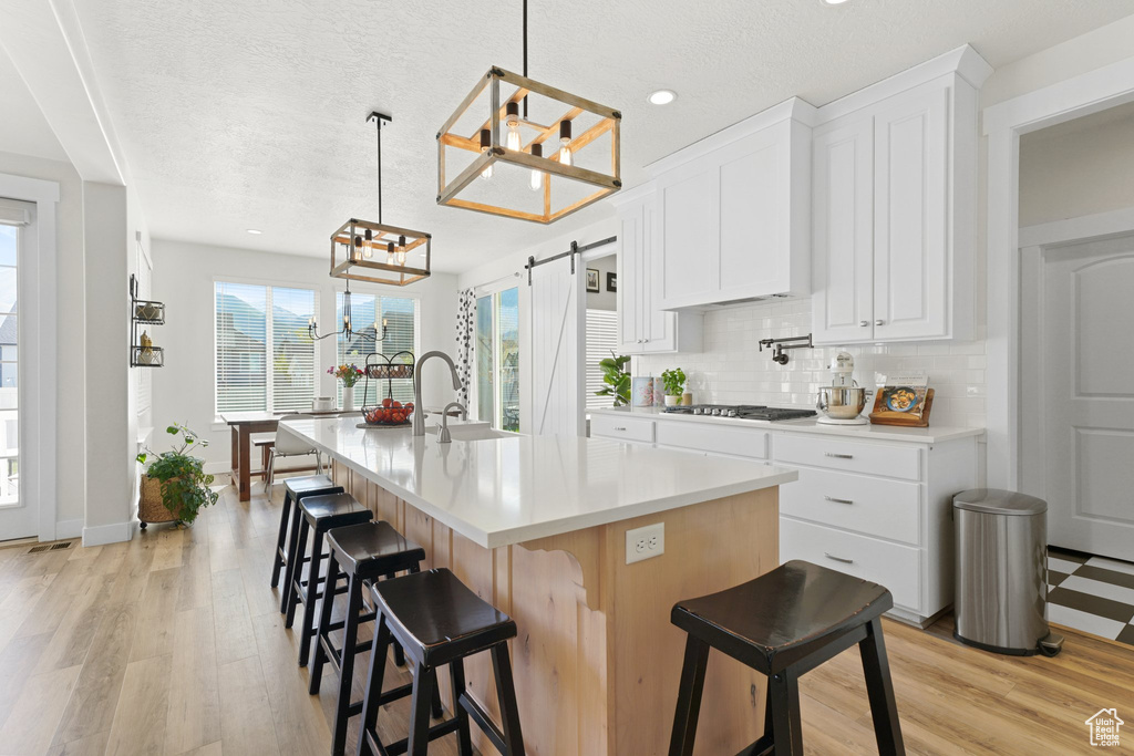 Kitchen with an island with sink, a barn door, white cabinets, light hardwood / wood-style flooring, and pendant lighting