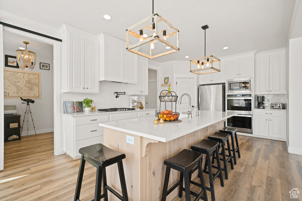 Kitchen featuring appliances with stainless steel finishes, light hardwood / wood-style flooring, hanging light fixtures, an island with sink, and a breakfast bar
