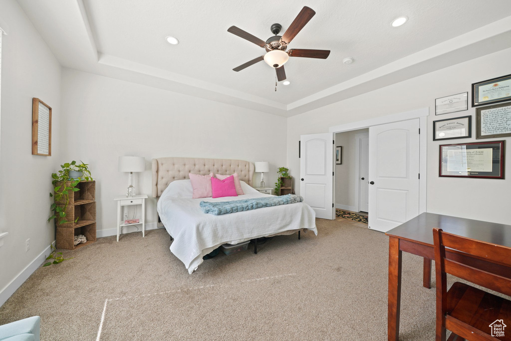 Bedroom with a raised ceiling, ceiling fan, and carpet flooring