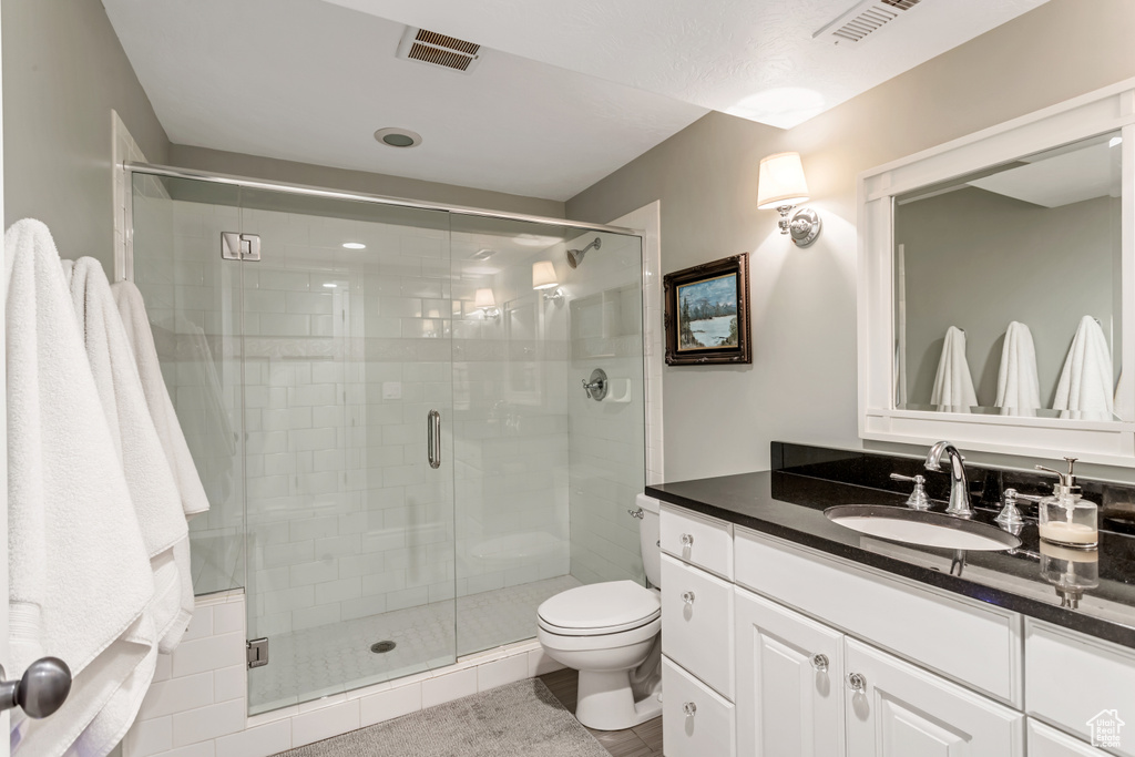 Bathroom featuring a shower with door, oversized vanity, tile floors, and toilet