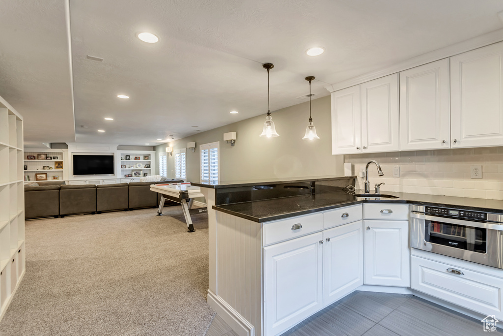 Kitchen with oven, sink, light carpet, white cabinetry, and pendant lighting