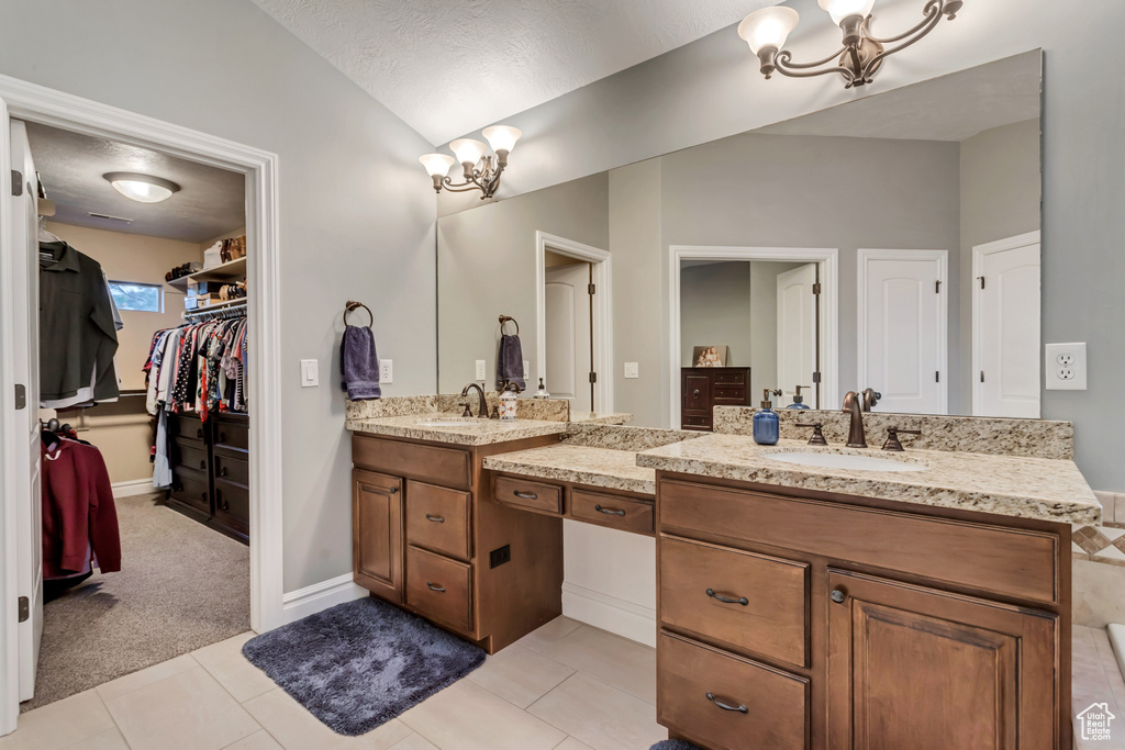 Bathroom with dual bowl vanity, tile floors, a notable chandelier, vaulted ceiling, and a textured ceiling