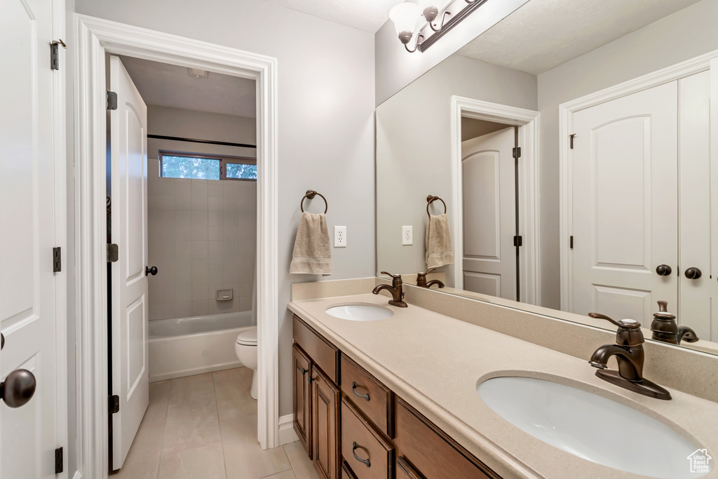 Full bathroom with tile flooring, vanity with extensive cabinet space, tiled shower / bath combo, dual sinks, and toilet