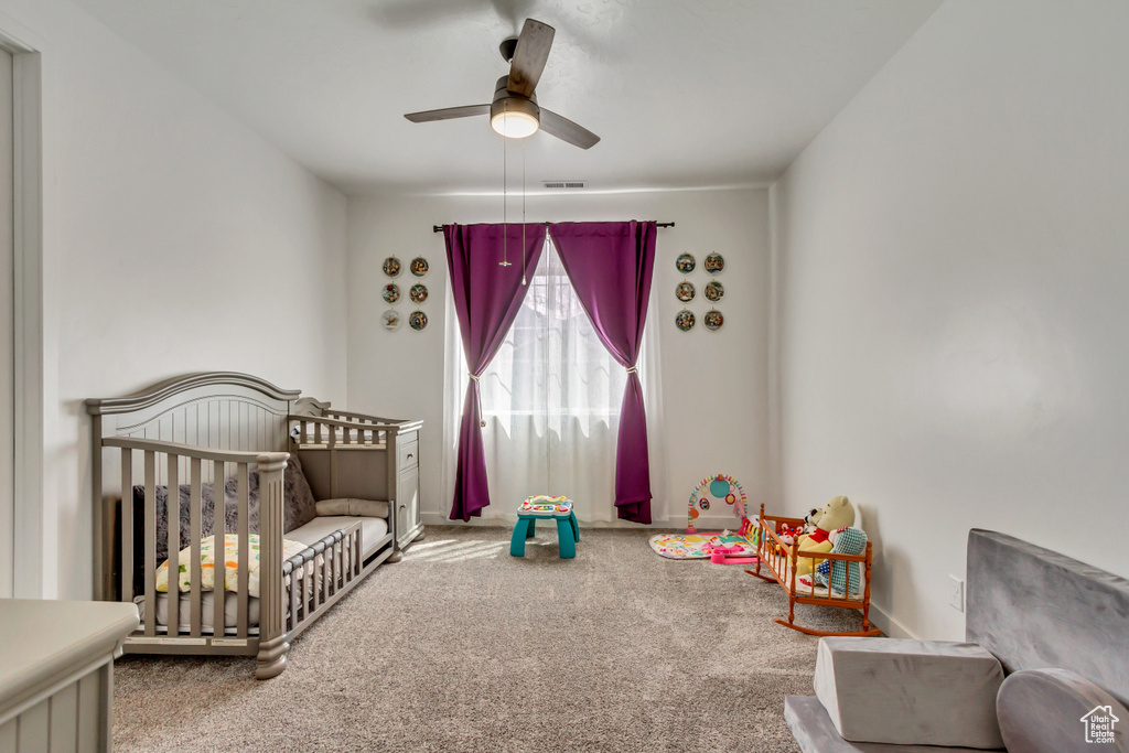 Carpeted bedroom featuring ceiling fan and a nursery area
