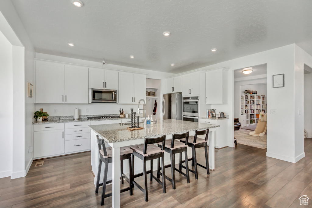 Kitchen featuring white cabinets, dark hardwood / wood-style floors, appliances with stainless steel finishes, sink, and an island with sink