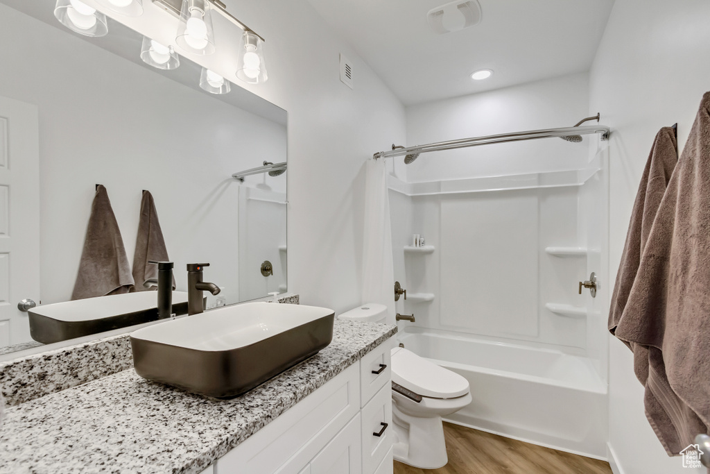 Full bathroom with shower / bathing tub combination, vanity with extensive cabinet space, hardwood / wood-style flooring, and toilet
