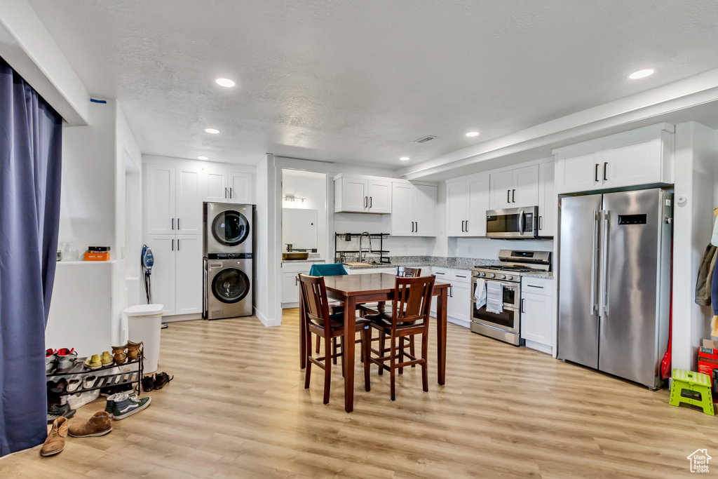 Kitchen featuring appliances with stainless steel finishes, light hardwood / wood-style flooring, stacked washing maching and dryer, and white cabinetry