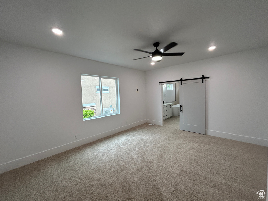 Unfurnished room with light carpet, ceiling fan, and a barn door