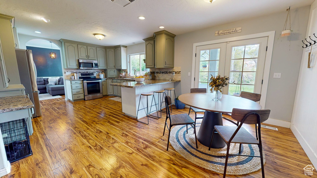 Kitchen featuring a healthy amount of sunlight, wood-type flooring, backsplash, kitchen peninsula, and stainless steel appliances
