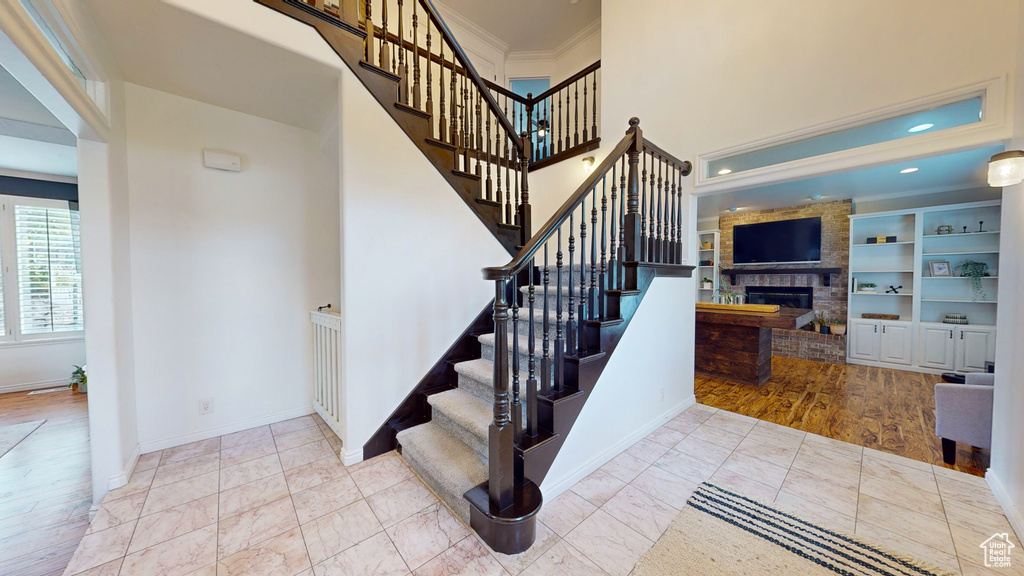 Stairway featuring built in features, light tile flooring, crown molding, and a stone fireplace