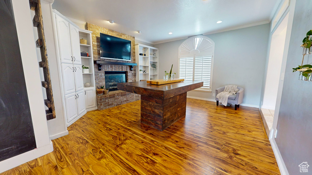 Home office featuring built in features, light hardwood / wood-style flooring, a brick fireplace, and crown molding