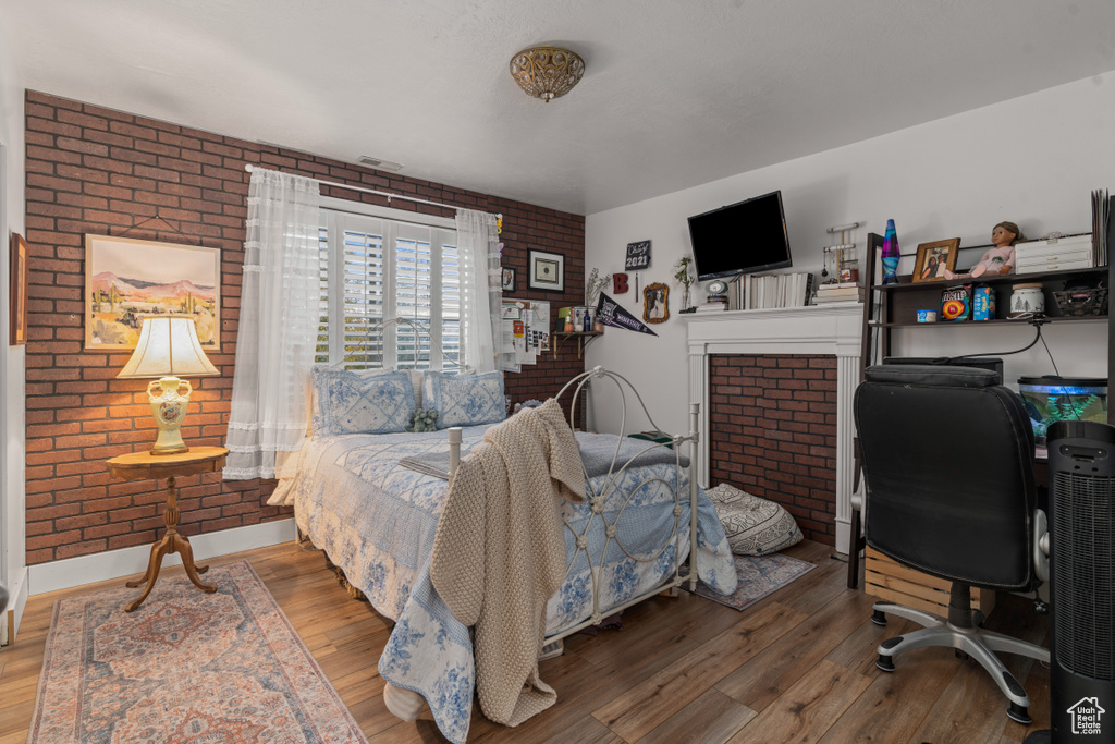Bedroom with hardwood / wood-style floors, brick wall, and a fireplace