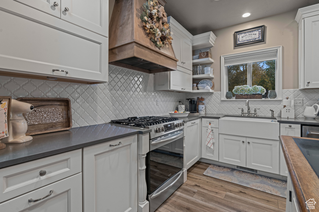 Kitchen featuring stainless steel range with gas stovetop, backsplash, white cabinetry, light hardwood / wood-style flooring, and custom range hood