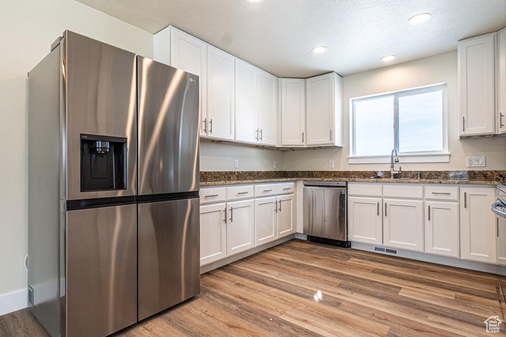 Kitchen with appliances with stainless steel finishes, sink, light hardwood / wood-style floors, and white cabinetry