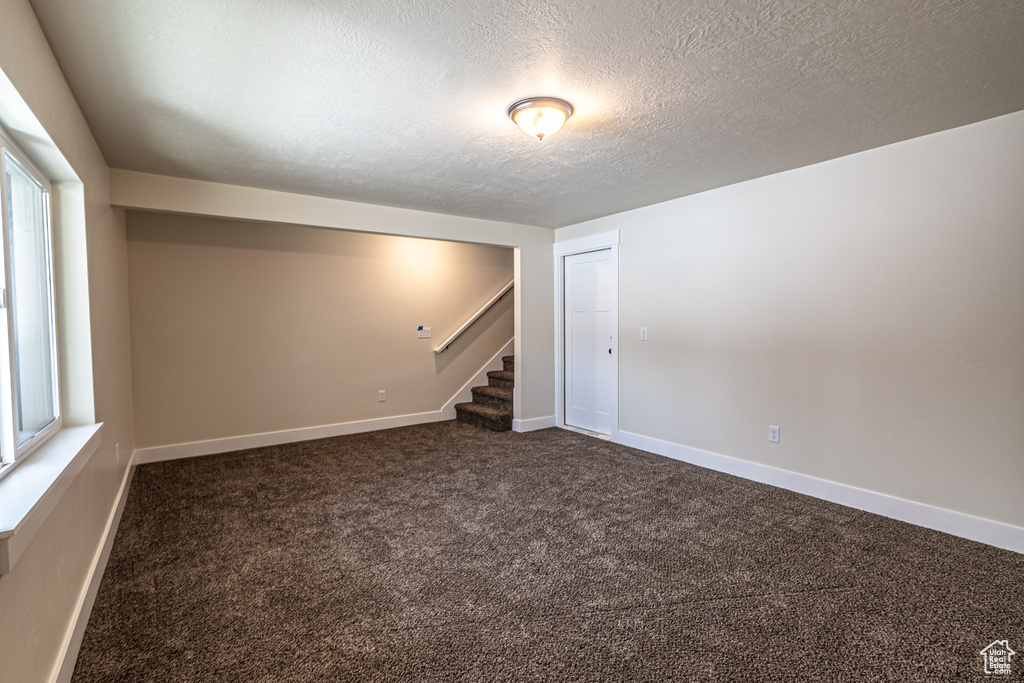 Unfurnished room featuring a textured ceiling, a wealth of natural light, and dark colored carpet