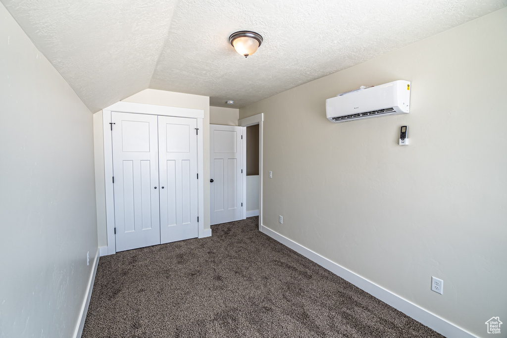 Unfurnished bedroom featuring a closet, a wall mounted air conditioner, a textured ceiling, and lofted ceiling