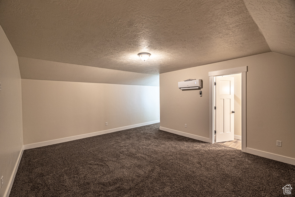 Spare room featuring lofted ceiling, an AC wall unit, carpet floors, and a textured ceiling