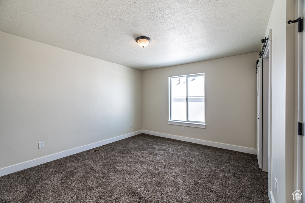 Empty room with dark colored carpet, a barn door, and a textured ceiling