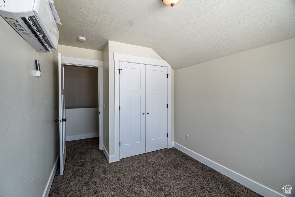 Unfurnished bedroom with a closet, a textured ceiling, dark carpet, and vaulted ceiling