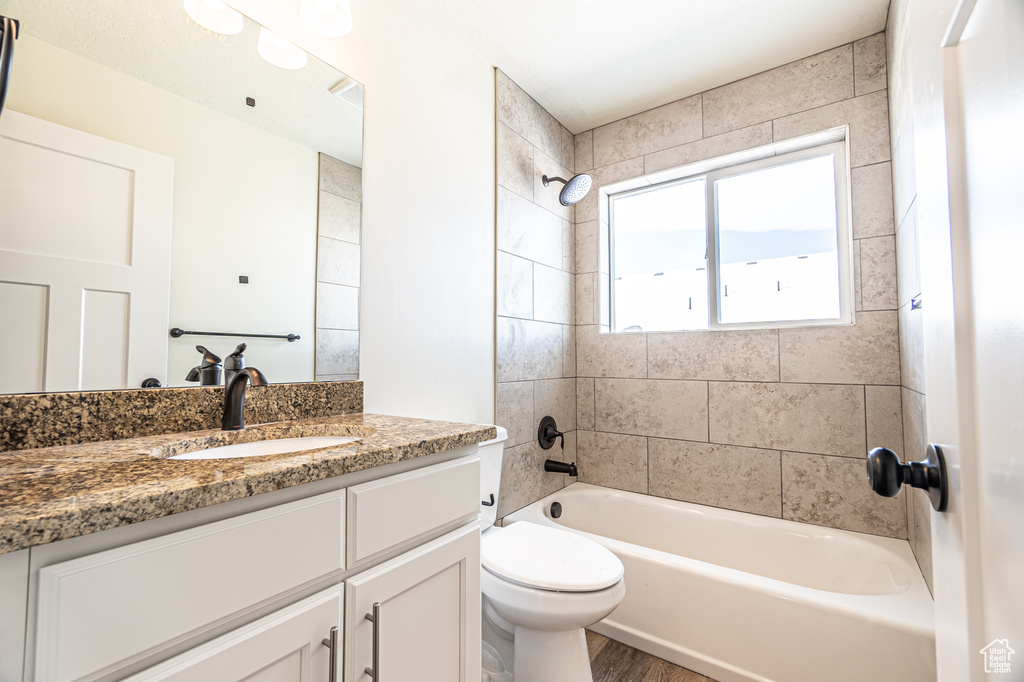 Full bathroom with hardwood / wood-style flooring, toilet, vanity with extensive cabinet space, and tiled shower / bath