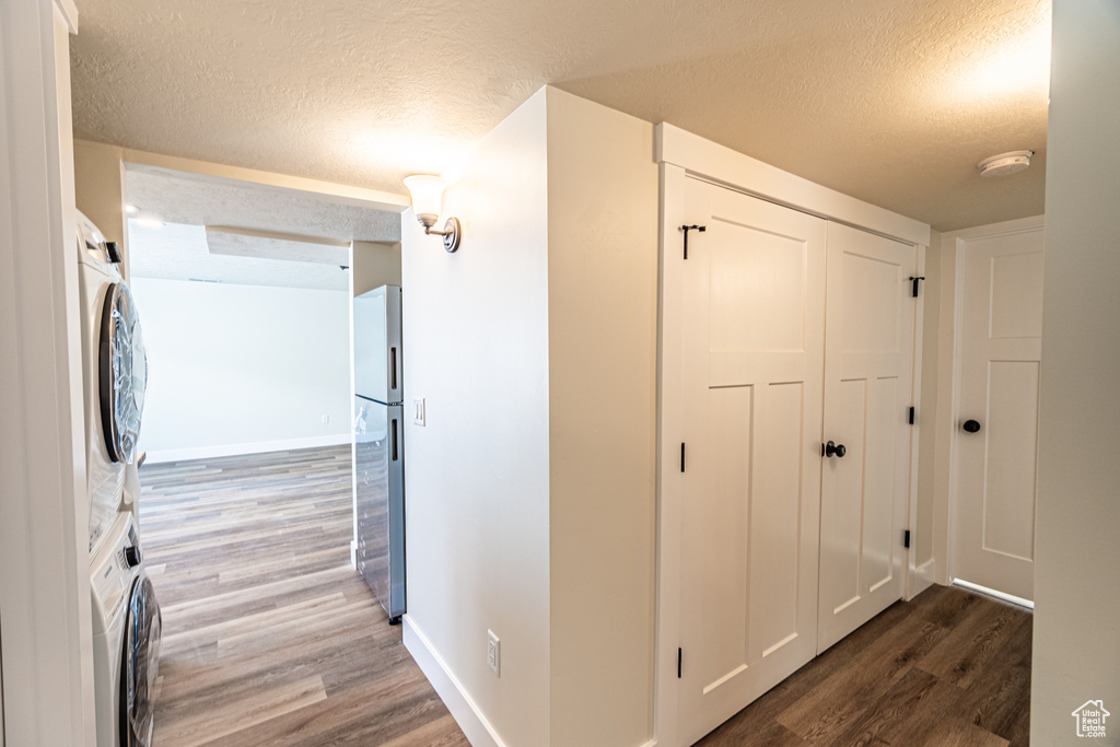 Corridor with a textured ceiling, hardwood / wood-style floors, and stacked washer and dryer