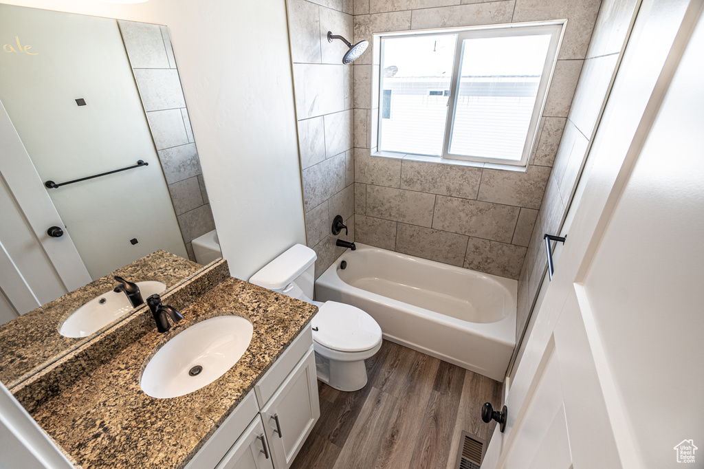 Full bathroom featuring tiled shower / bath combo, large vanity, toilet, and hardwood / wood-style flooring