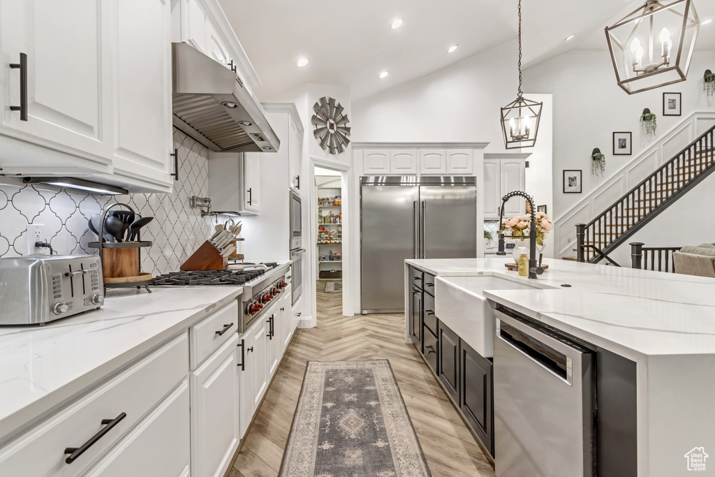 Kitchen featuring wall chimney exhaust hood, white cabinetry, appliances with stainless steel finishes, vaulted ceiling, and tasteful backsplash