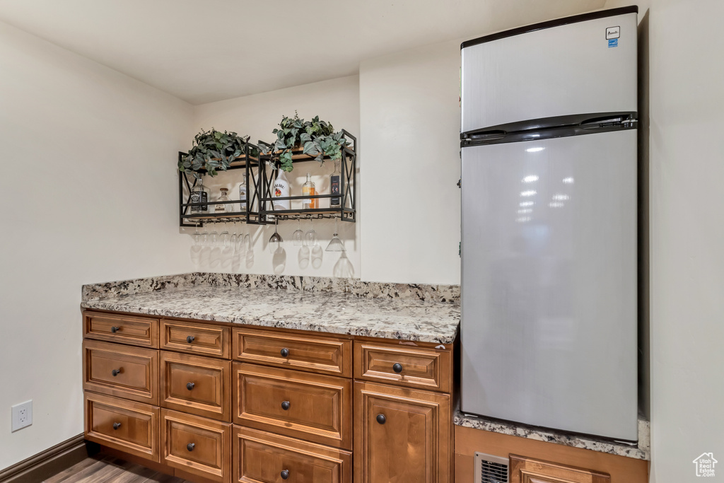 Kitchen featuring dark hardwood / wood-style flooring, stainless steel fridge, and light stone countertops