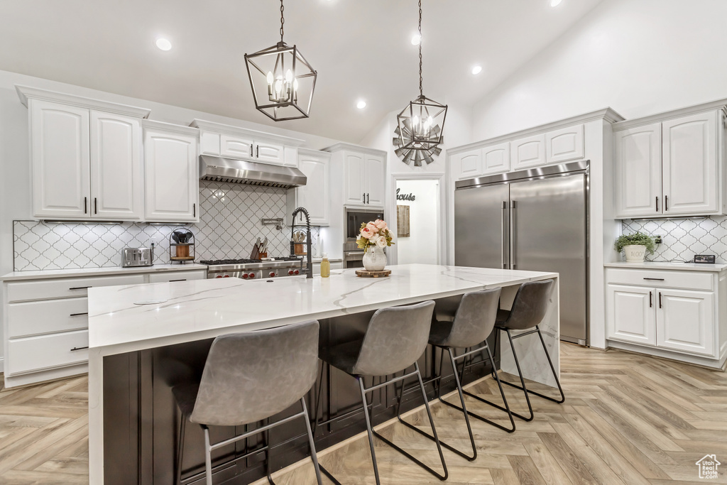 Kitchen featuring light parquet flooring, a kitchen island with sink, and built in appliances