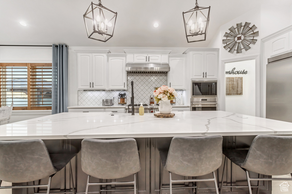 Kitchen featuring a large island, appliances with stainless steel finishes, white cabinets, and light stone counters