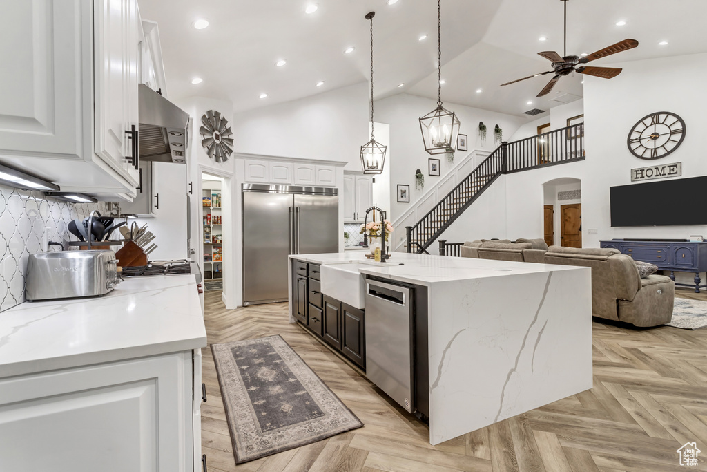 Kitchen with light parquet flooring, appliances with stainless steel finishes, high vaulted ceiling, white cabinetry, and a kitchen island with sink
