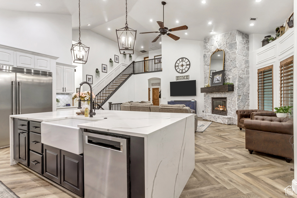 Kitchen with high vaulted ceiling, light parquet floors, stainless steel appliances, a stone fireplace, and ceiling fan