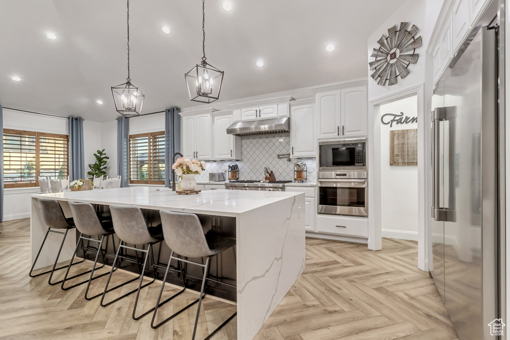 Kitchen with light stone counters, stainless steel appliances, a spacious island, and light parquet flooring