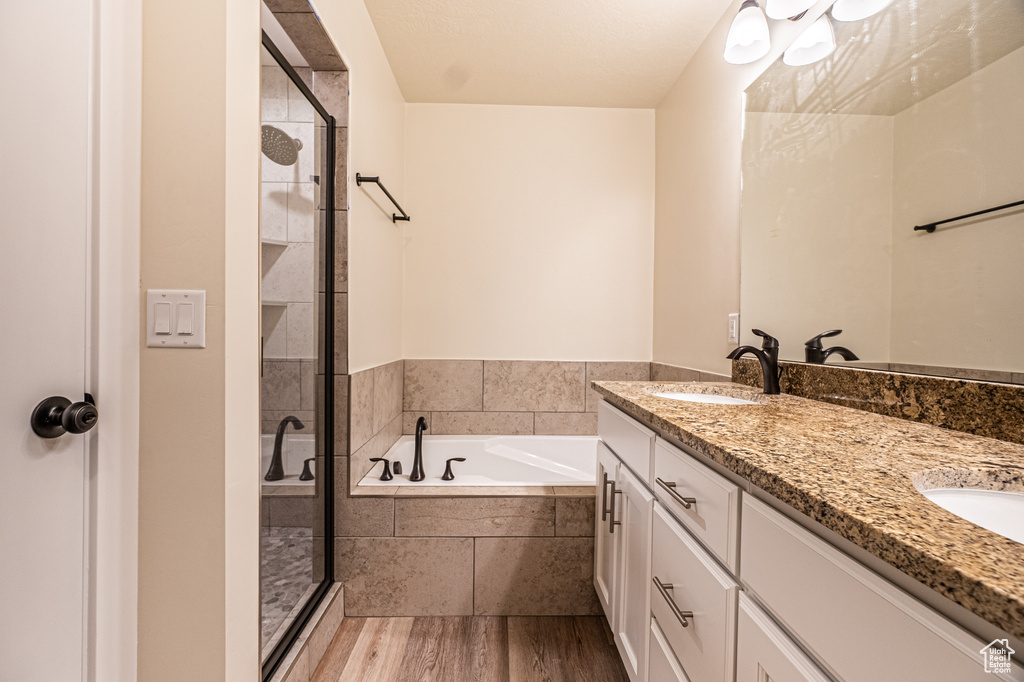 Bathroom with double sink, shower with separate bathtub, hardwood / wood-style floors, and large vanity