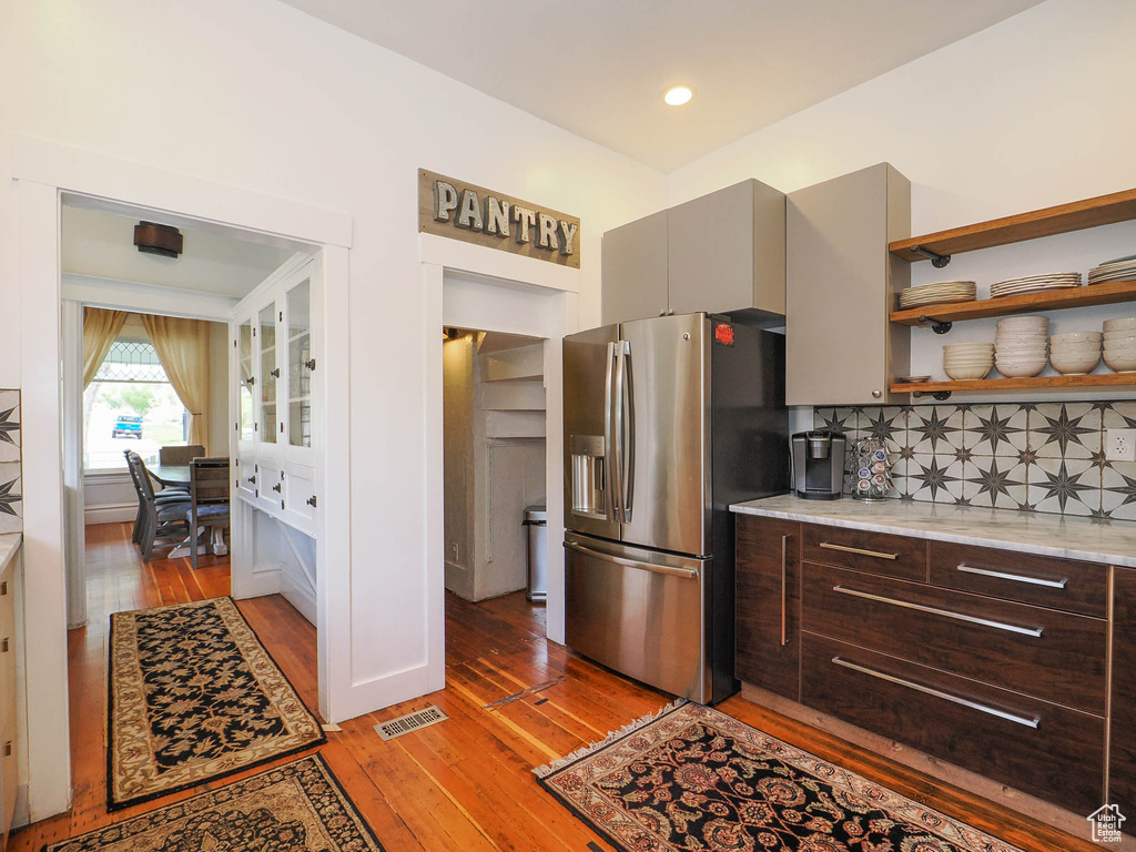 Kitchen featuring light wood-type flooring, light stone countertops, dark brown cabinetry, backsplash, and stainless steel fridge