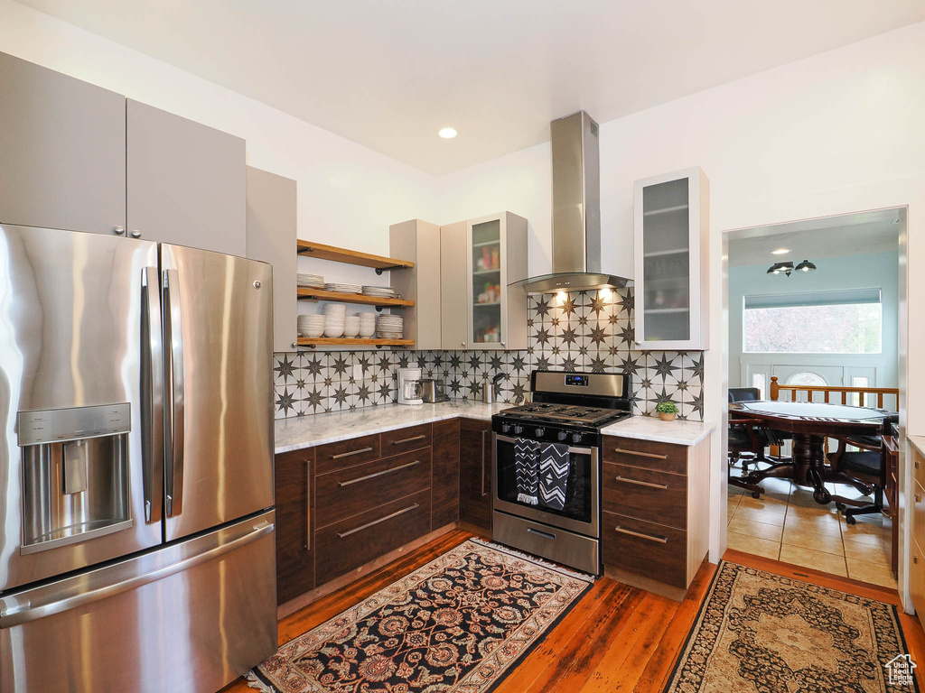 Kitchen featuring wall chimney exhaust hood, dark brown cabinets, stainless steel appliances, and backsplash