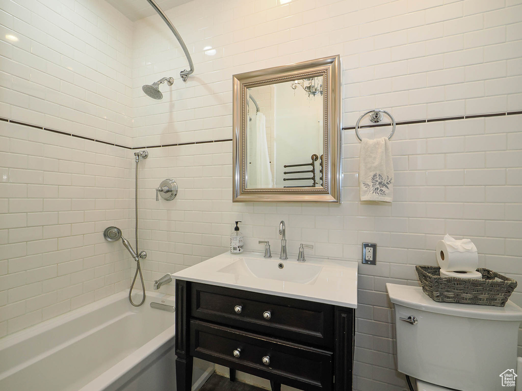 Full bathroom featuring tiled shower / bath, vanity, toilet, and tile walls