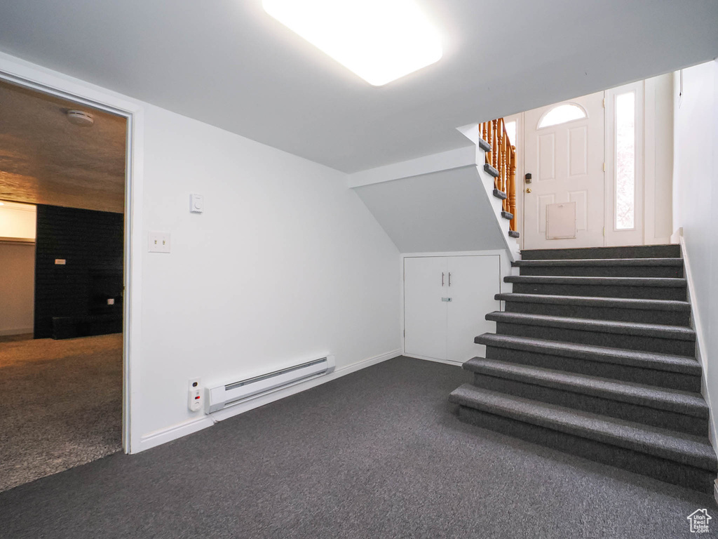 Stairway with vaulted ceiling, dark carpet, and a baseboard heating unit