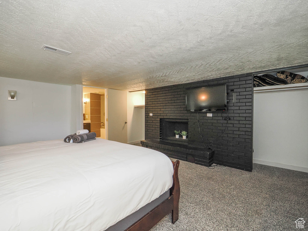 Carpeted bedroom with a textured ceiling, brick wall, and a brick fireplace