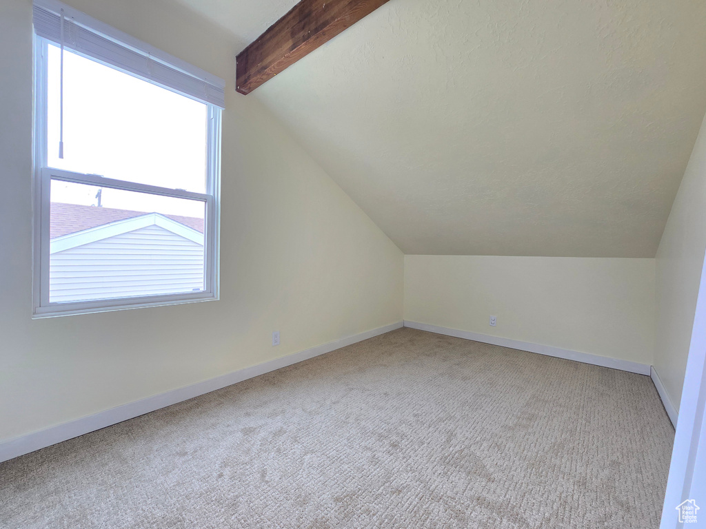 Additional living space with a healthy amount of sunlight, vaulted ceiling with beams, and carpet floors