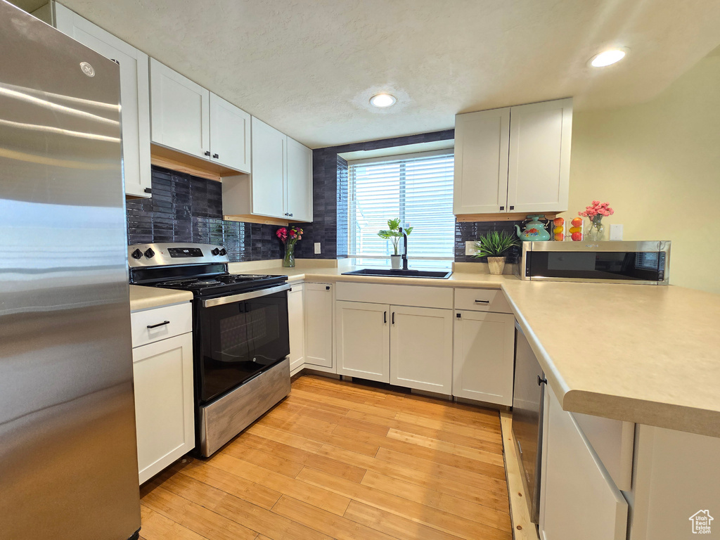 Kitchen with sink, backsplash, white cabinetry, stainless steel appliances, and light hardwood / wood-style flooring